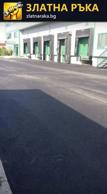 Тъмна асфалтова настилка пред редица складови входове със зелени врати.