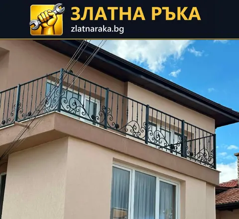 Черен метален парапет с извити орнаменти по дълъг балкон на светла двуетажна къща