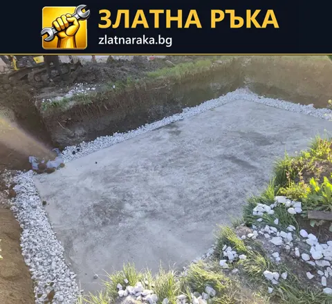 Правоъгълна бетонна площадка е обрамчена с бели камъчета до ниска стена и градински растения
