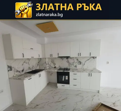 Бяла ъглова кухня с горни шкафове, вградена фурна и светъл гръб с мраморен рисунък