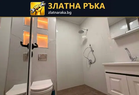 Светла баня със стъклен душ параван, бял шкаф и две топло осветени стенни ниши.