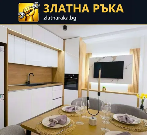 Бяла кухня с дървесен гръб и високи шкафове до трапезна маса и телевизионна зона с ламели