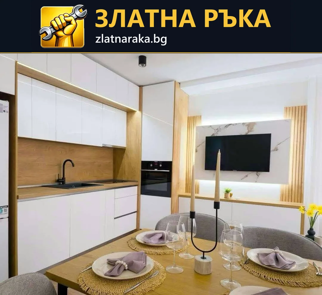 Бяла кухня с дървесен гръб и високи шкафове до трапезна маса и телевизионна зона с ламели