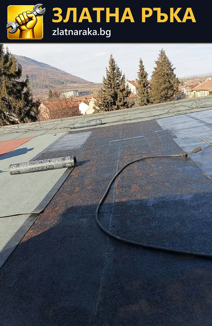 Плосък покрив е покрит на части с тъмен рулонен материал, с маркуч и незавършени участъци по повърхността
