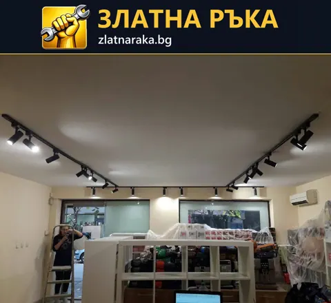 Две черни таванни шини с насочени прожектори над покрити стелажи в помещение с витрини