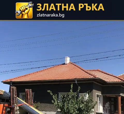 Къща с червен многоскатен керемиден покрив, широки стрехи и комин над тъмна фасадна повърхност