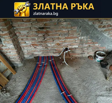 Група червени и сини защитени тръбни линии по пода, изведени към оголена тухлена стена.
