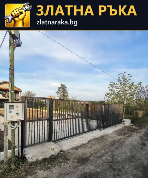 Черна метална ограда с вертикални пръти върху ниска бетонна основа покрай двор и път