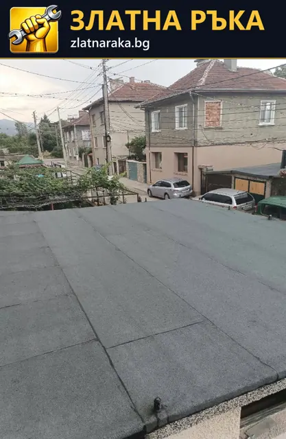 Сиво рулонно покритие с прави надлъжни фуги върху нисък покрив пред съседни къщи