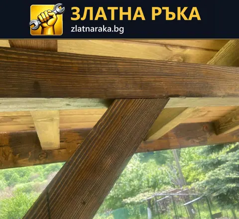 Близък кадър на дървен възел под навес с хоризонтална греда, наклонена подпора и видима дървесна шарка.