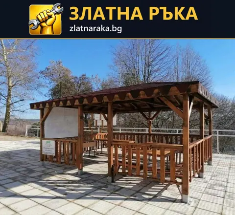 Завършена дървена беседка с парапет и покрив върху площадка от квадратни плочи.
