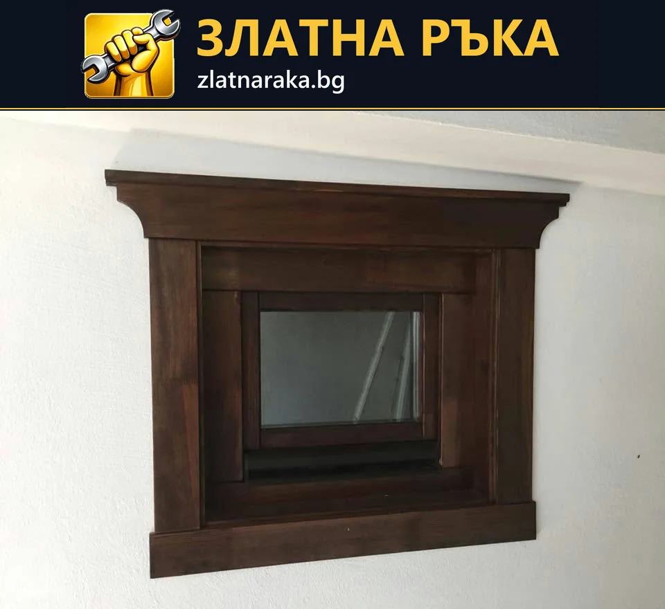 Малък прозорец с масивна тъмнокафява декоративна рамка и широк горен профил.