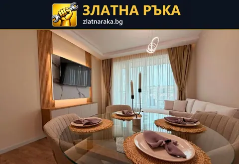Дневна с трапезарна маса, светъл диван, дървесна телевизионна стена и топло скрито осветление.