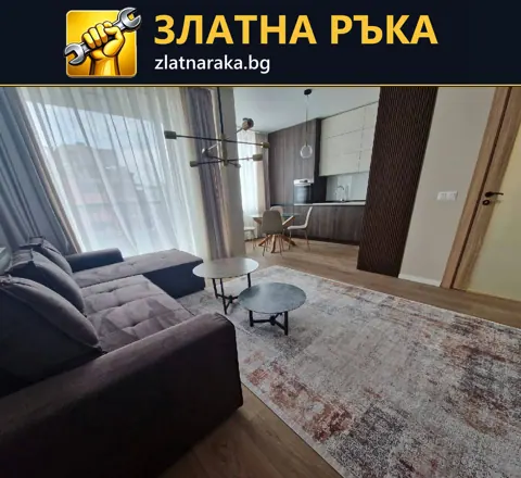 Светла дневна с тъмен ъглов диван, голям килим и кухненска зона зад ниски холни маси