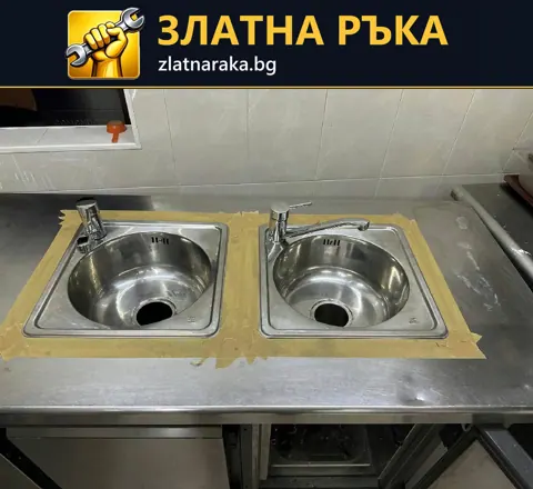 Две отделни метални мивки със смесители са вградени една до друга в широк метален плот