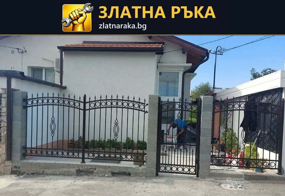 Черни метални оградни пана с вертикални пръчки и орнаменти между светли колони пред бяла къща