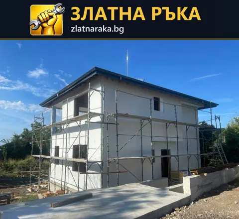 Двуетажна къща със светла фасада и монтирано скеле по външните стени