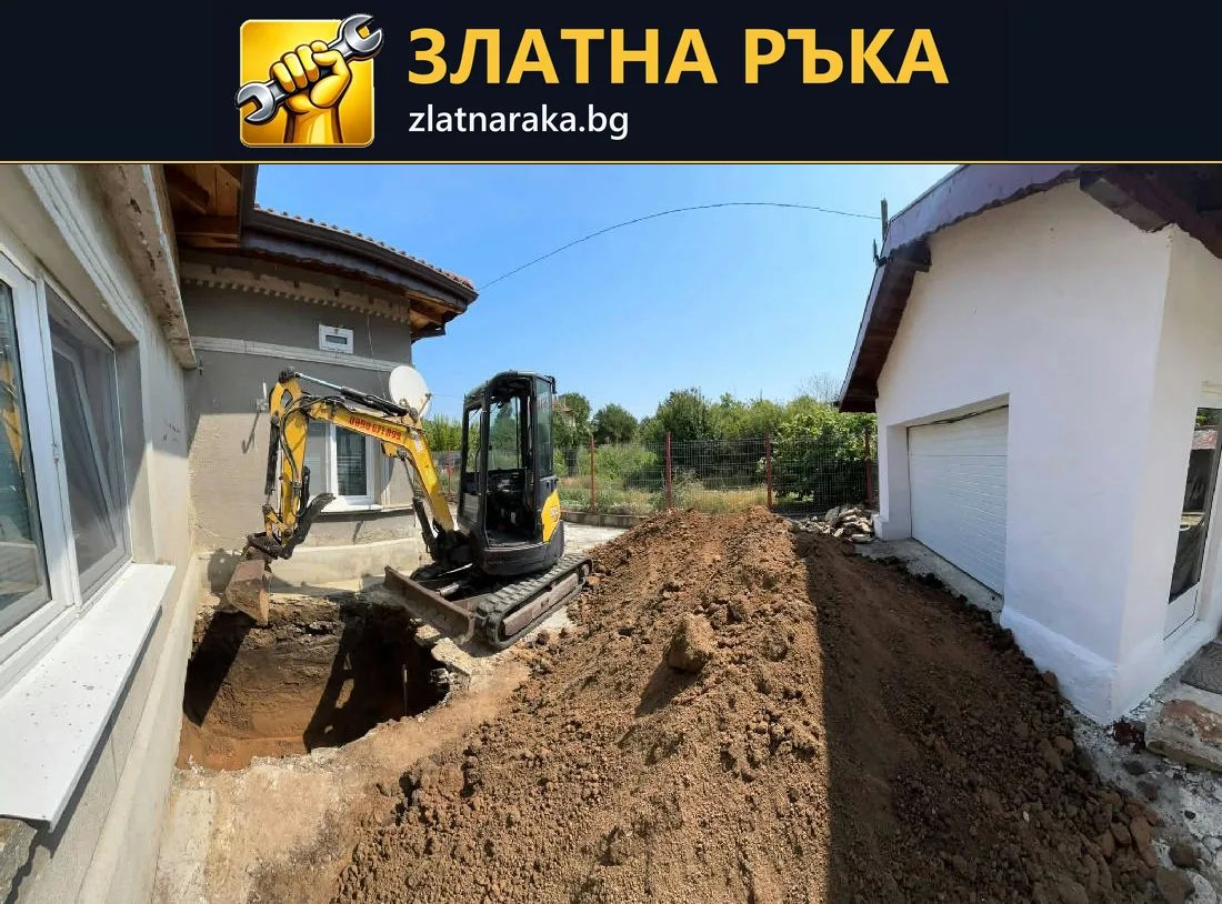 Малък багер до открит изкоп и натрупана почва между две светли сгради