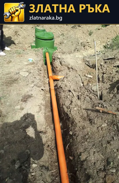 Оранжева канализационна тръба в открит изкоп, свързана към зелена ревизионна шахта.