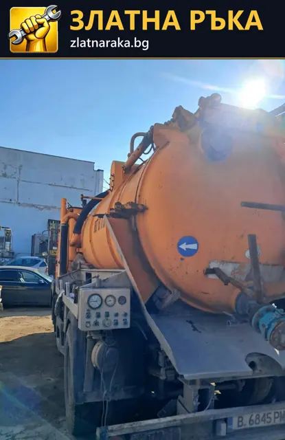 Оранжев специализиран автомобил с голям заден резервоар и маркучи е паркиран до промишлена сграда