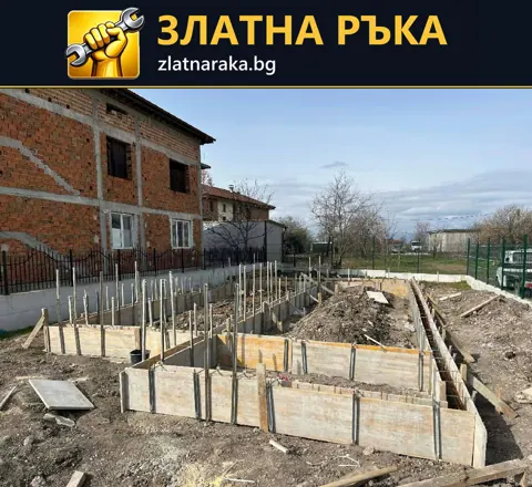 Ниски кофражни стени очертават основи с вертикални армировъчни пръти в открит строителен изкоп
