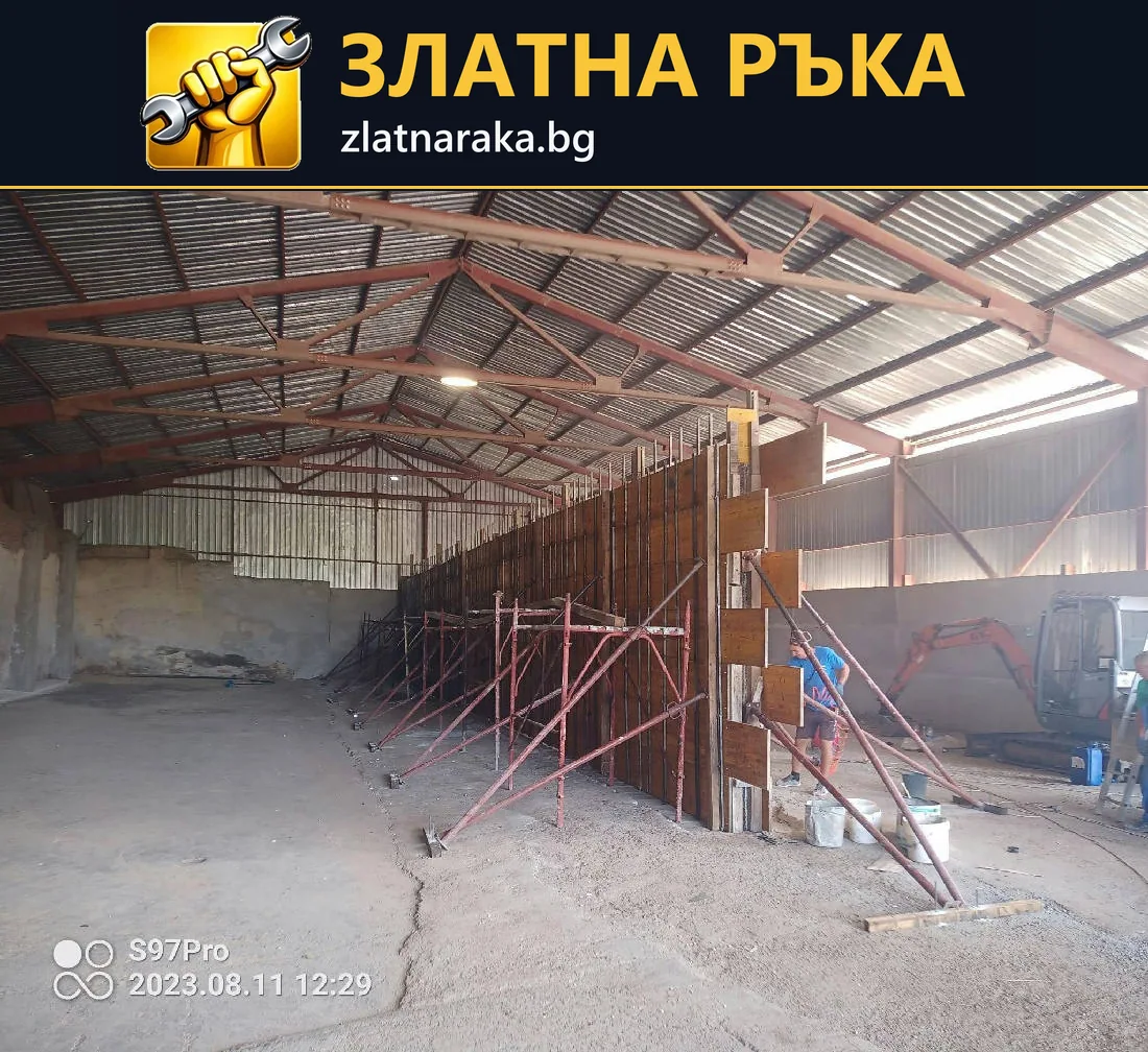 Дълъг дървен кофраж с метални подпори под откритата покривна конструкция на хале.