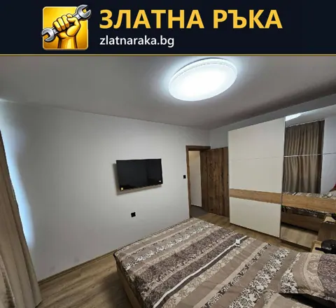 Обзаведена спалня с голям гардероб, стенен телевизор и кръгло таванно осветление.