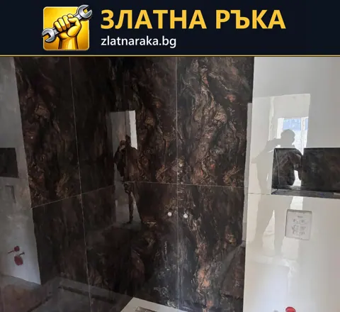 Контрастна баня в ремонт с тъмна гланцова облицовка с жилки и бели съседни участъци.