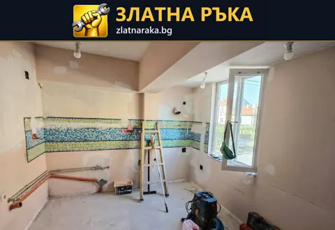Празна кухня по време на ремонт с цветна ивица стари плочки, видими тръби и стълба до прозореца