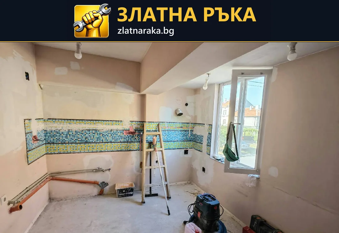 Празна кухня по време на ремонт с цветна ивица стари плочки, видими тръби и стълба до прозореца