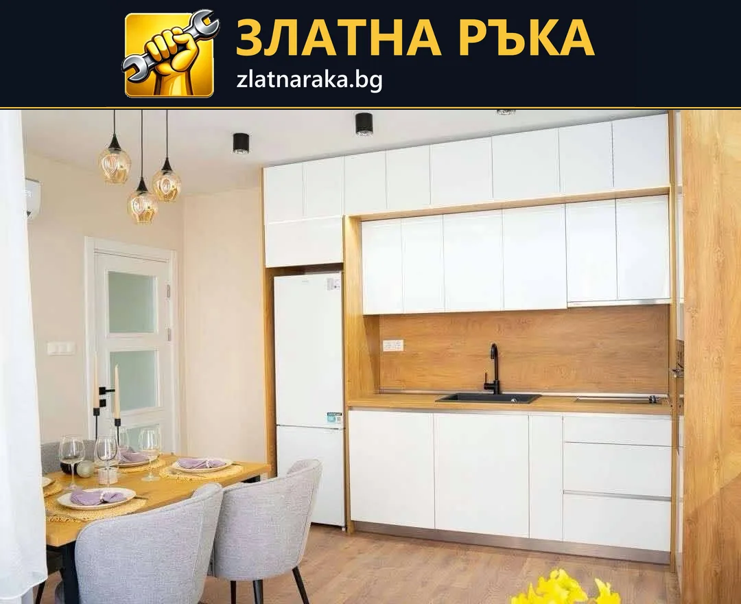 Линейна кухня с бели фронтове, дървесен гръб, черен смесител и хладилник до малка трапезна маса