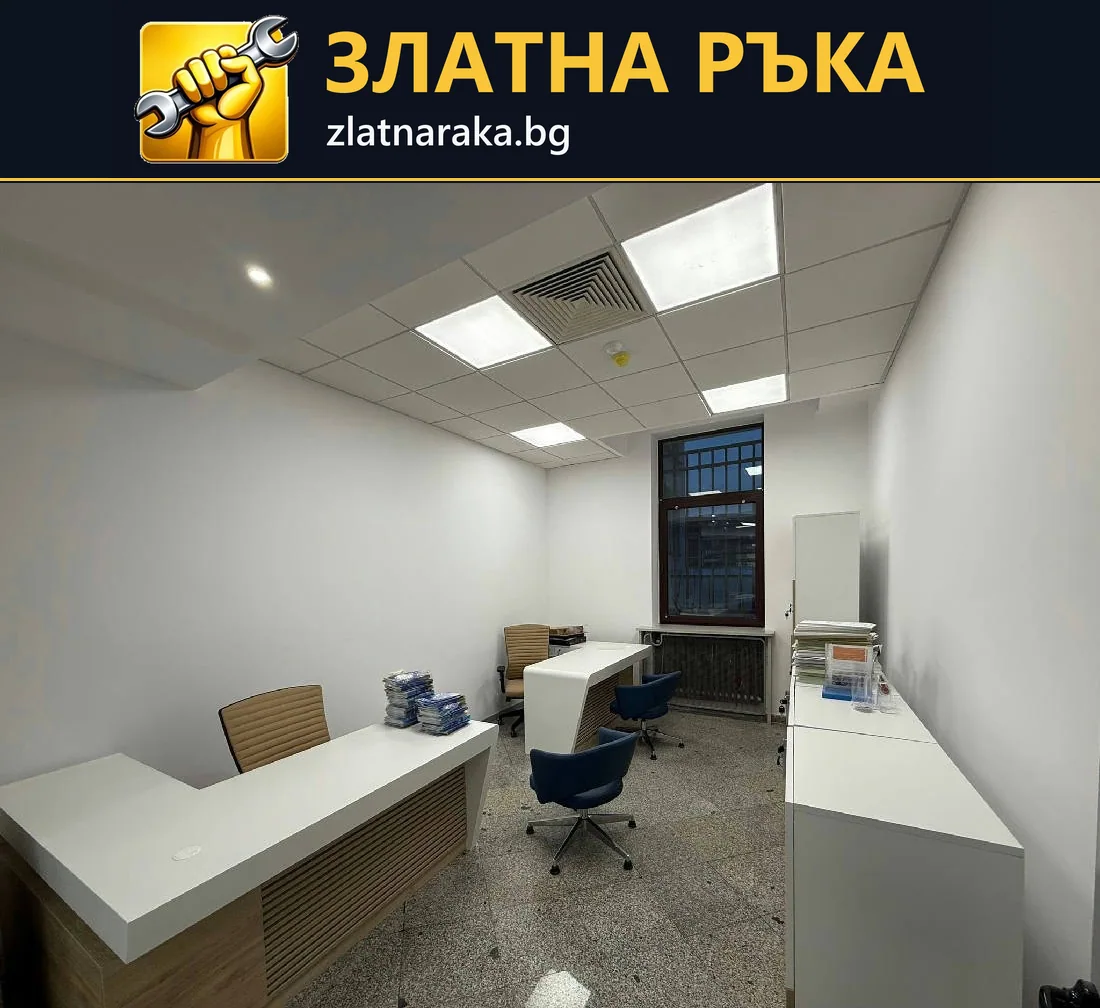 Компактно офис помещение с бели работни бюра, син стол и светлинни панели в окачен модулен таван