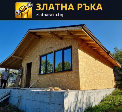 Ниска постройка с дървесни плоскости, тъмна дограма и открита дървена стреха.
