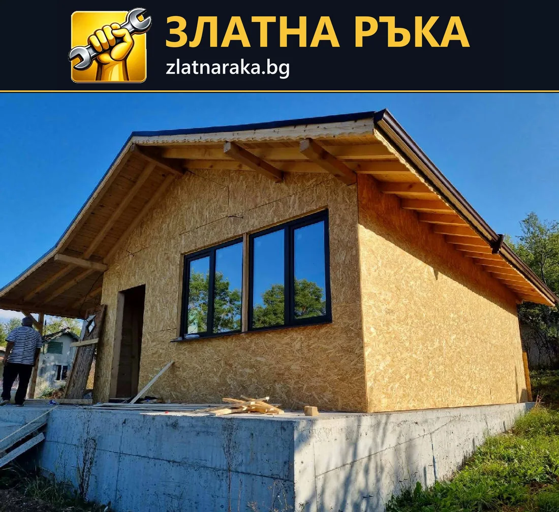Ниска постройка с дървесни плоскости, тъмна дограма и открита дървена стреха.