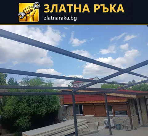 Открити метални колони и хоризонтални греди над площадка между ниски постройки.