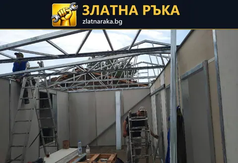 Метални покривни ферми над затворено помещение със стенни панели, стълби и монтажници.