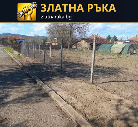 Нова мрежеста ограда върху метални колове край улица и неозеленен двор.