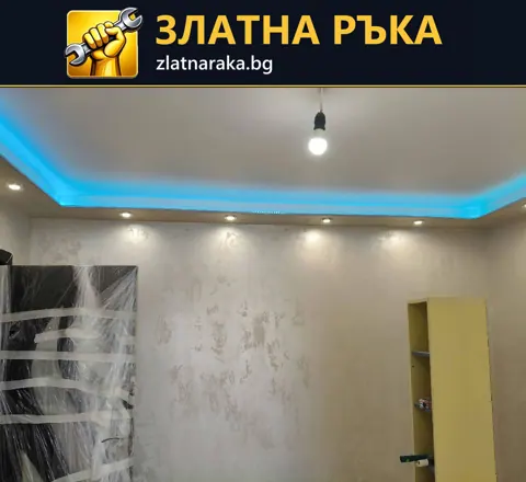 Окачен таван със синьо периферно осветление и спотове над стена с декоративна текстура.