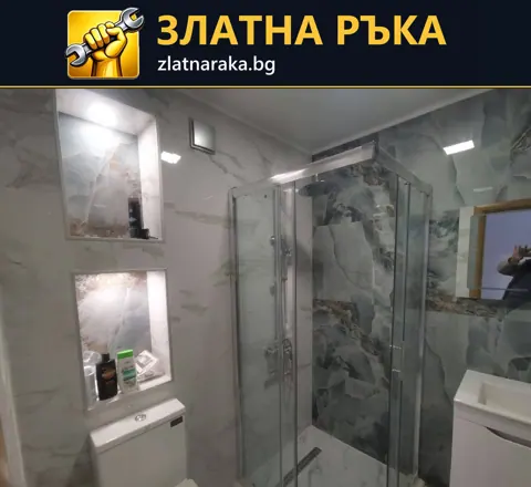 Малка баня с остъклен душов кът, осветени ниши, светли плочки и вградена тоалетна зона.