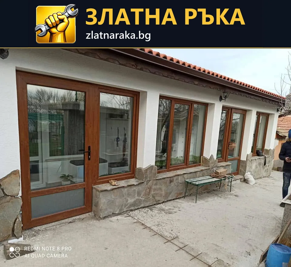 Дълга остъклена фасада с кафява дограма, прозорци и входна врата пред каменен цокъл.