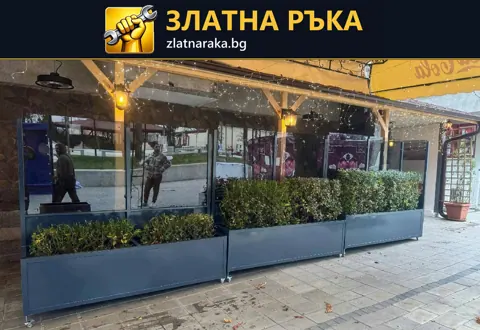 Ред тъмносиви правоъгълни кашпи пред остъклена тераса с дървена козирка