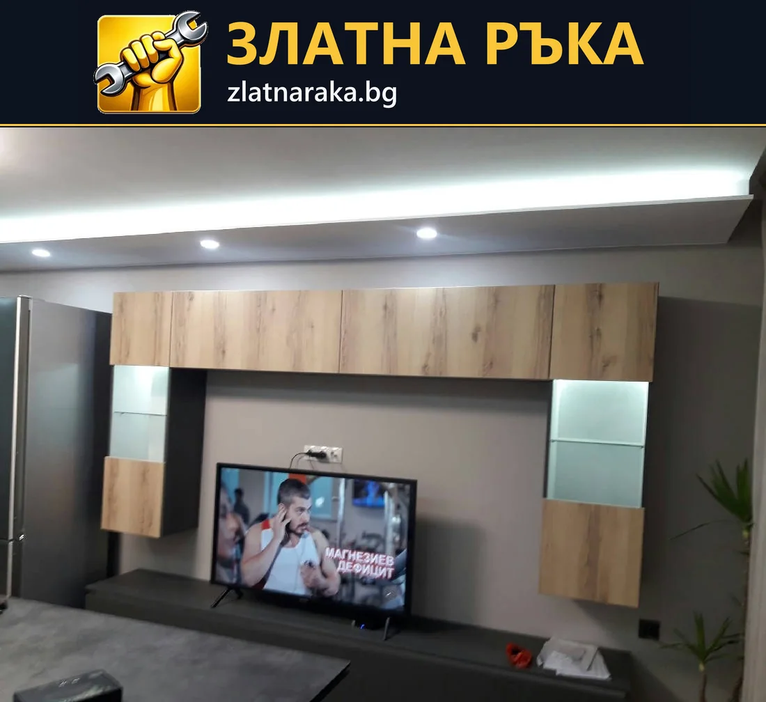 Телевизионна секция с дървесни шкафове, осветени стъклени витрини и светла линия по тавана над нея
