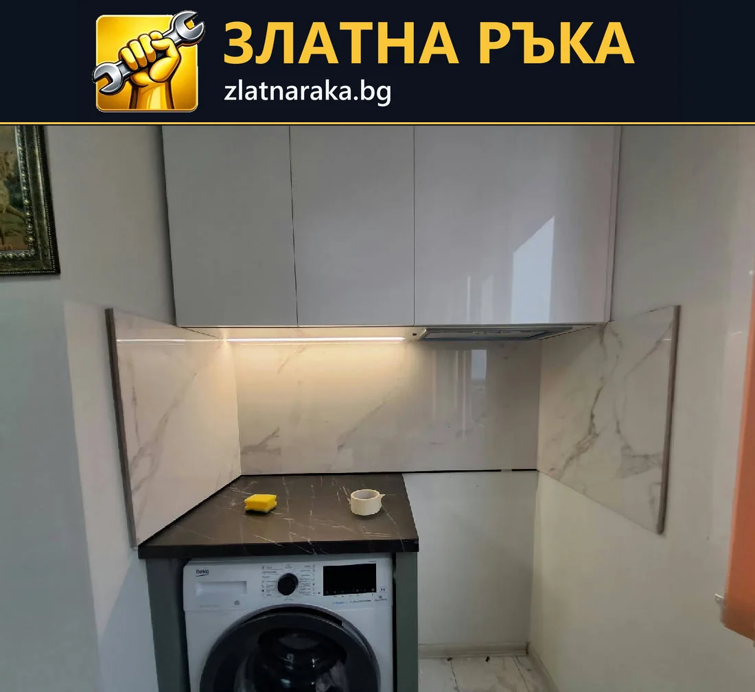 Перална зона с уред под тъмен плот, бели горни шкафове и светъл гръб с жилки.