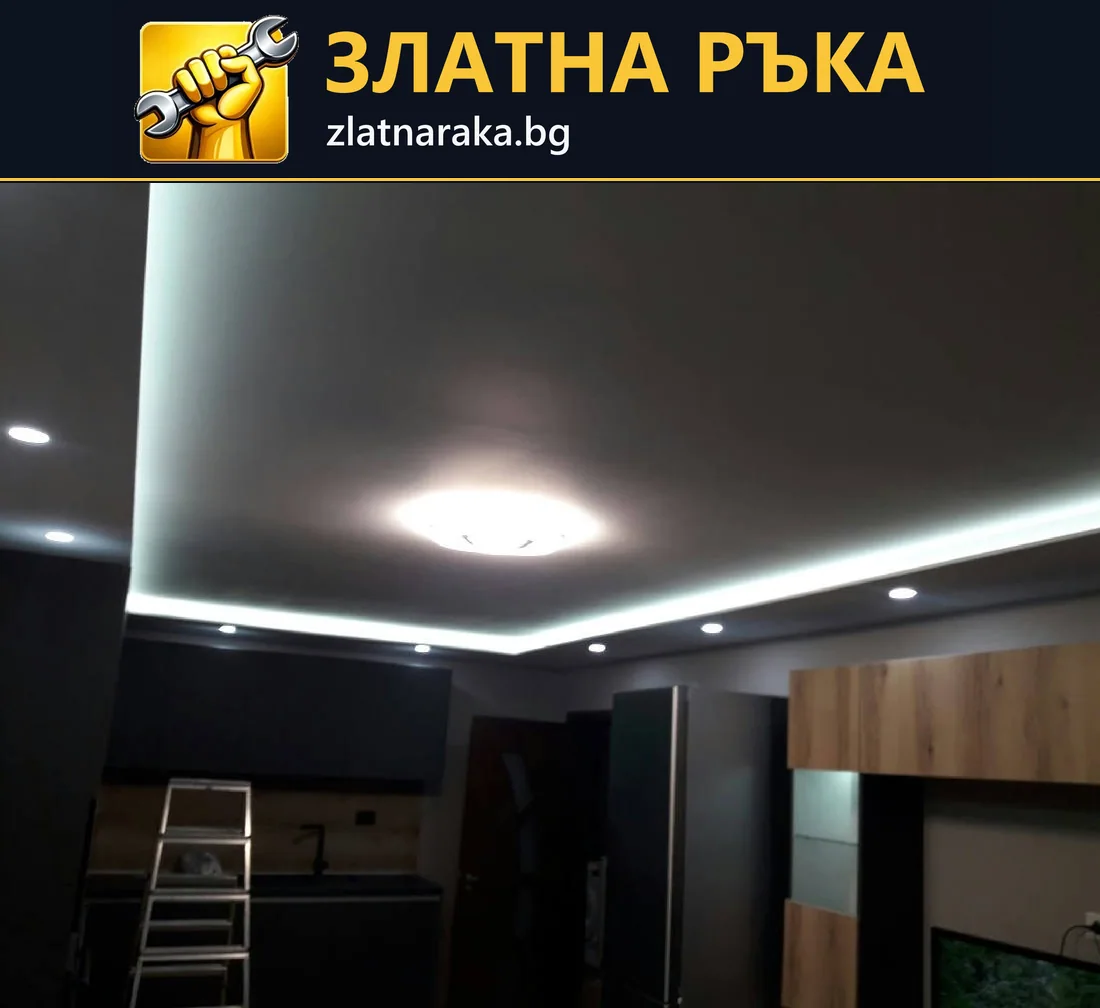 Тъмен таван със светла периферна линия, вградени лунички и централно осветително тяло над кухня