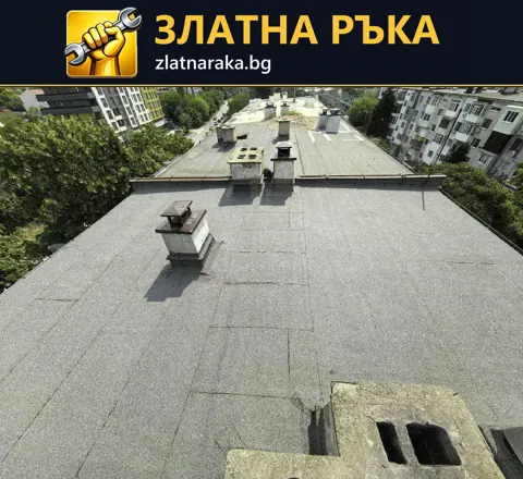 Широк плосък покрив със сиво рулонно покритие и няколко коминни тела.