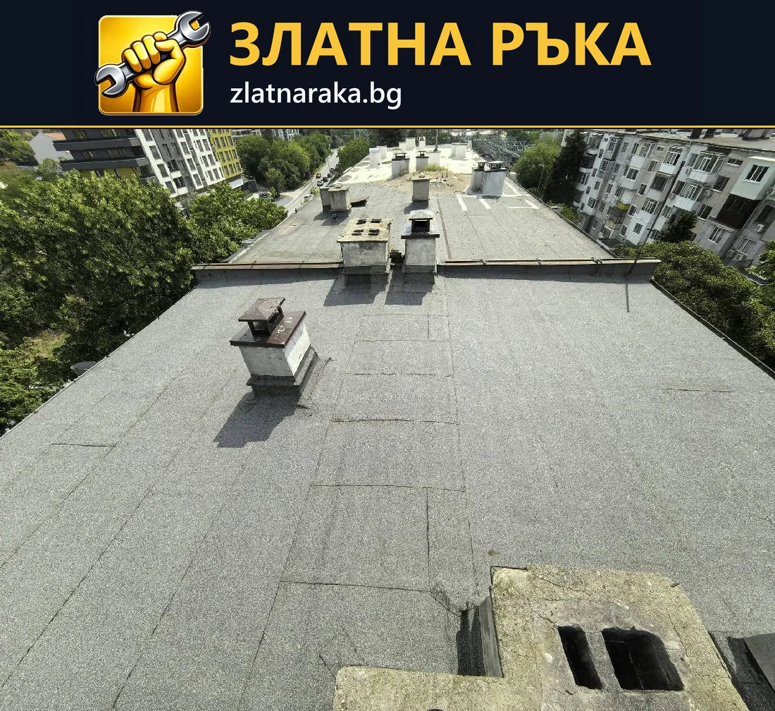 Широк плосък покрив със сиво рулонно покритие и няколко коминни тела.