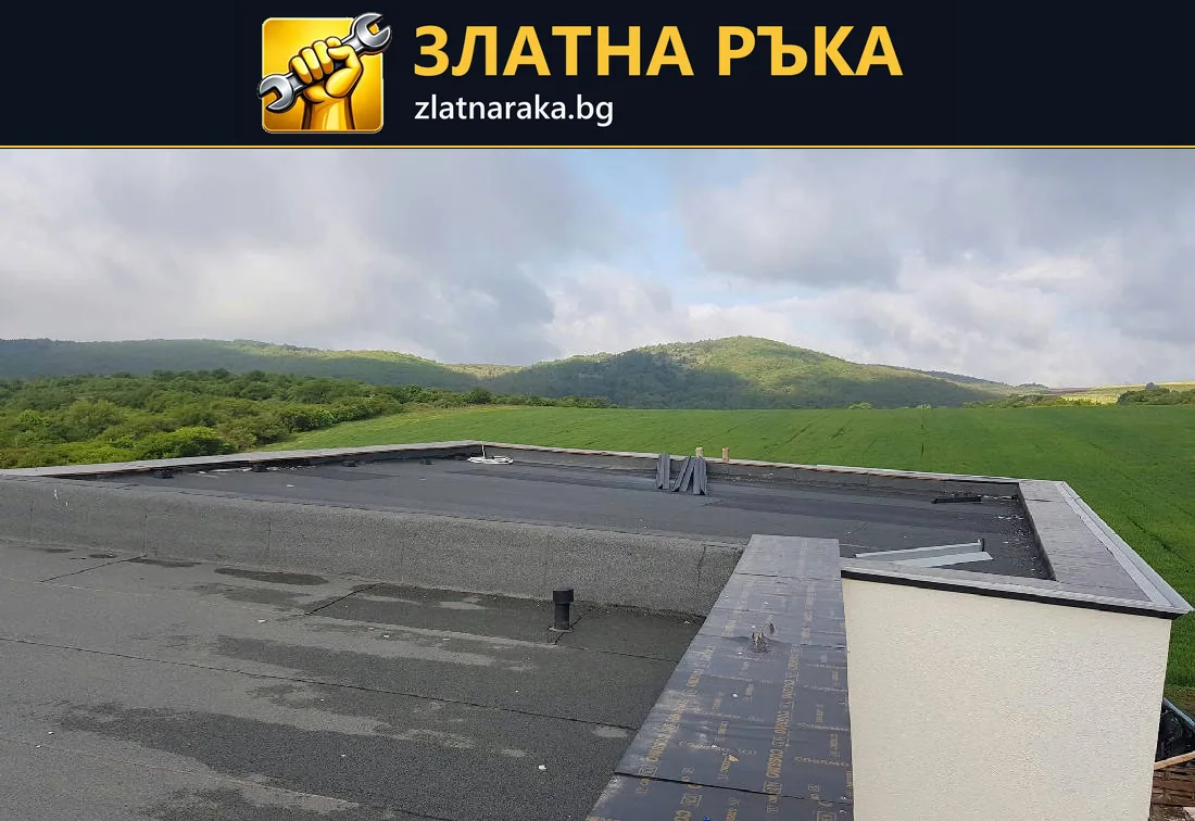Плосък покрив с тъмна хидроизолация и светли периферни бордове на сграда сред открит терен.