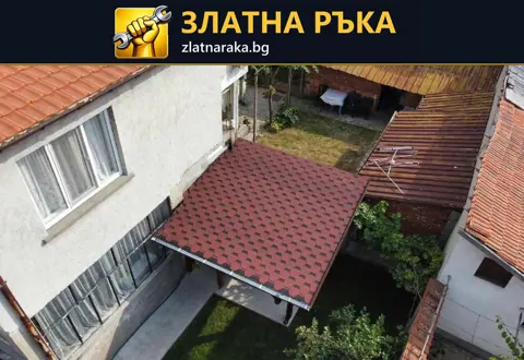 Правоъгълен червен покрив на дворен навес между светлата фасада на къща и съседна постройка