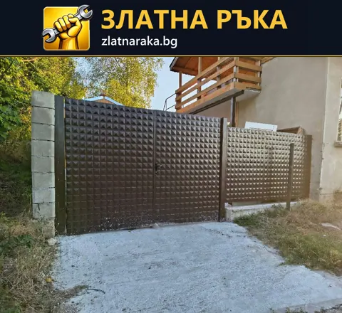 Кафява метална порта и съседно оградно пано с повтарящ се релеф между светли колони