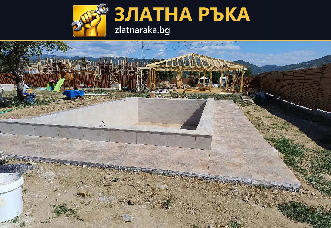 Правоъгълна бетонна вана в двор с настилка около нея и дървена конструкция отзад.